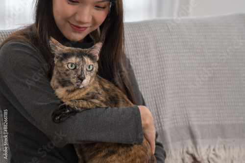 Принти на полотні woman kneeling beside a couch, playfully interacting with her tortoiseshell cat sitting on the couch