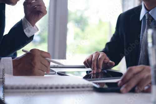 Two businessmen sitting at tbale, using tigital tablet and laptop co-working at modern office, close up. Business colleagues working together, having a discussion on a project photo