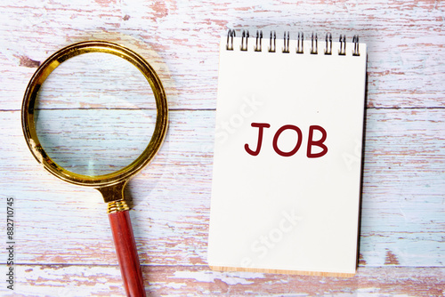 Job search and job hunting concept. A word JOB in a notebook next to a magnifying glass on old boards photo