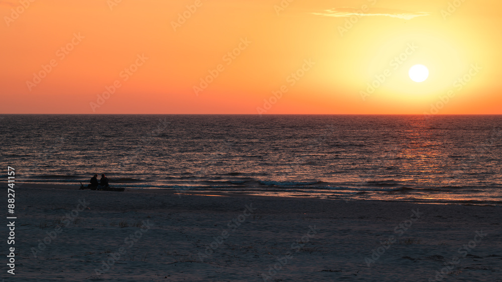 Beautiful sunset over the Baltic Sea. Silhouettes of two people on the beach watching the sunset. Slajszewo, Poland
