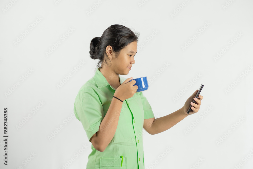 young Asian nurse looking at cell phone while drinking coffee and looking happy, isolated white background
young Asian nurse looking at cell phone while drinking coffee and looking happy, isolated white background
