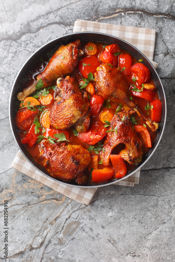 Slow stew rooster in tomato gravy with vegetables close-up in a pan on the table. Vertical top view from above