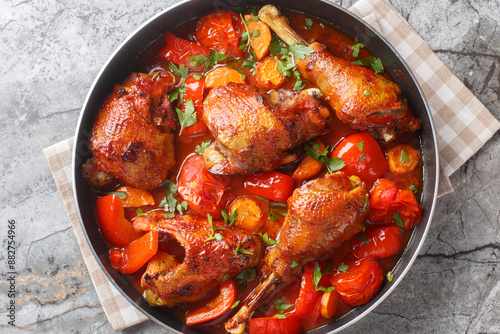 Slow cooked rooster with bell peppers, onions and carrots in tomato sauce close-up in a pan on the table. Horizontal top view from above