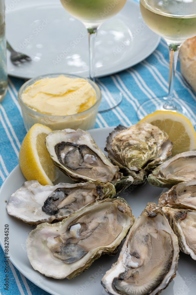 Plate with fresh live oysters with citron, bread, butter and white wine served at restaurant in oyster-farming village, Arcachon bay, Gujan-Mestras port, France Plate with fresh live oysters with citron, bread, butter and white wine served at restaurant in oyster-farming village, Arcachon bay, Gujan-Mestras port, France