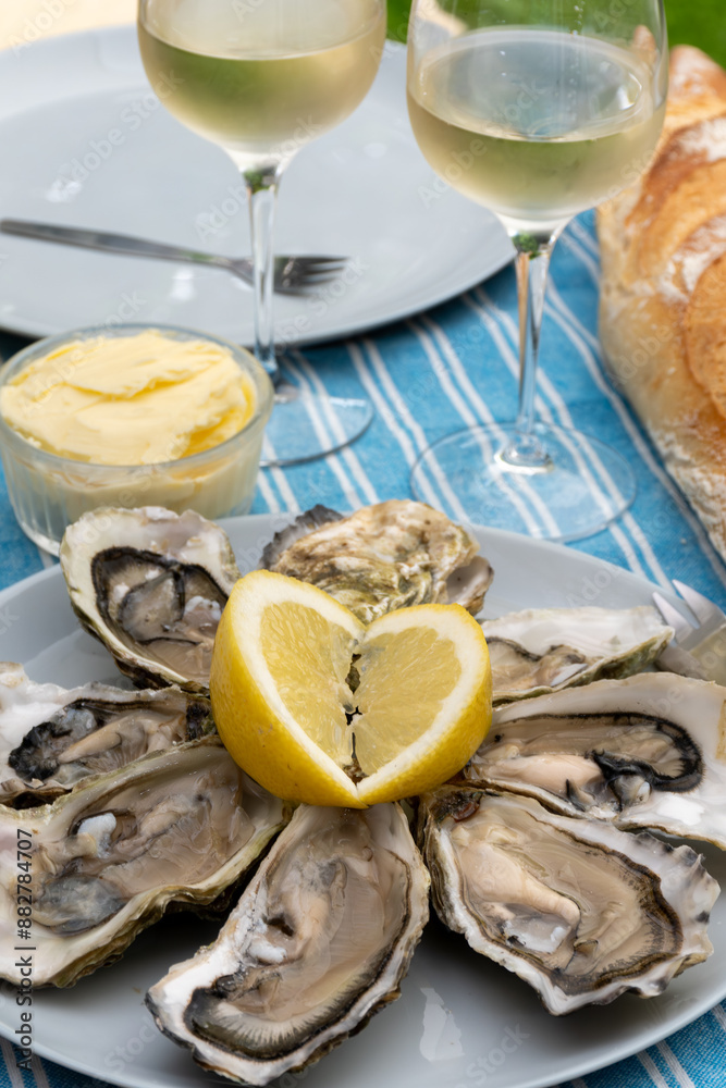 Plate with fresh live oysters with citron, bread, butter and white wine served at restaurant in oyster-farming village, Arcachon bay, Gujan-Mestras port, France Plate with fresh live oysters with citron, bread, butter and white wine served at restaurant in oyster-farming village, Arcachon bay, Gujan-Mestras port, France