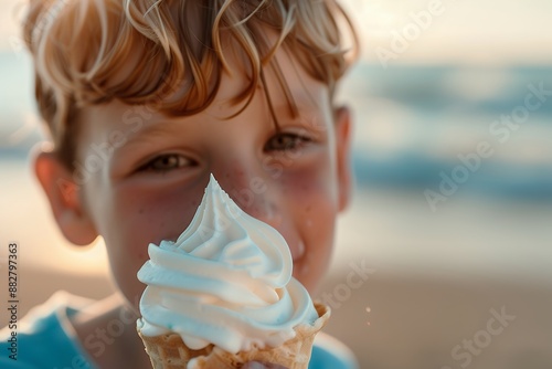 A young boy eating an ice cream cone with white soft serve in it, in a close up shot focused on the gelato and child's face, with a blurred background of a beach setting in the warm lighting of a summ photo