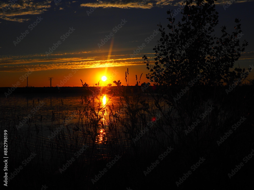 Fototapeta premium Sunset in hues of reddish-orange and yellow over the lake on a summer day.