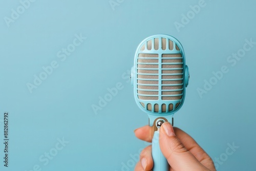 Close-up of a hand holding a vintage blue microphone against a light blue background.