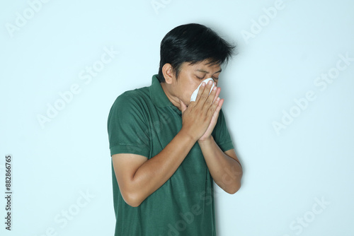 Young Asian man cover his nose and mouth with tissue when sneezing. Wearing a green t-shirt