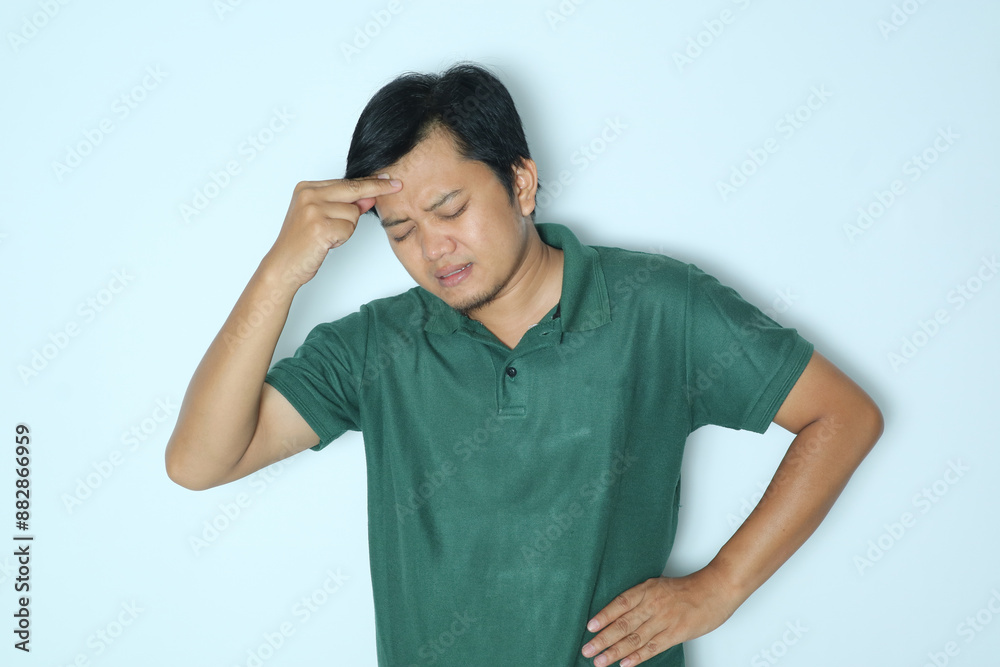 Young Asian man showing pain expression while touching the right side of his head. Wearing a green t-shirt Young Asian man showing pain expression while touching the right side of his head. Wearing a green t-shirt