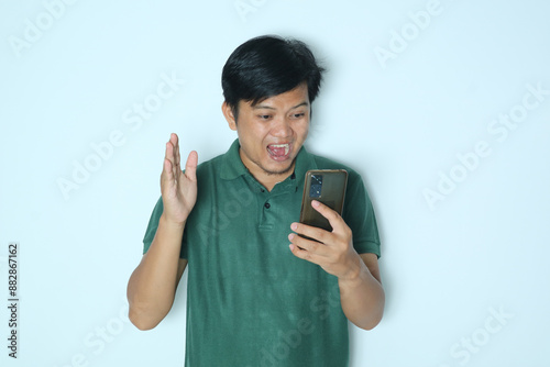 Young Asian man looking to his mobile phone with wow expression. Wearing a green t-shirt photo