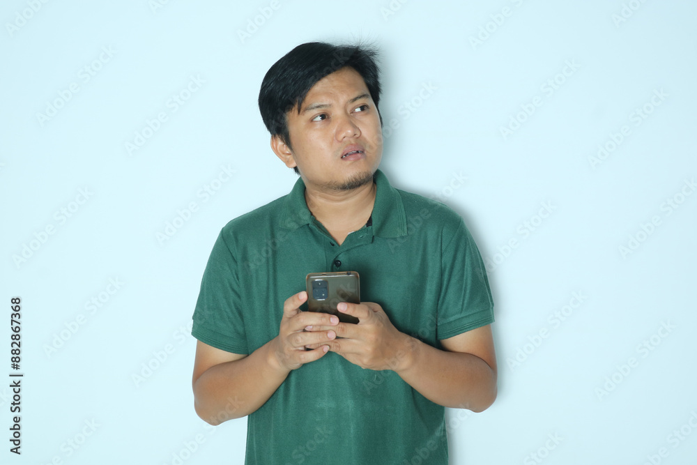 Young Asian man think something while typing on his mobile phone. Wearing a green t-shirt Young Asian man think something while typing on his mobile phone. Wearing a green t-shirt