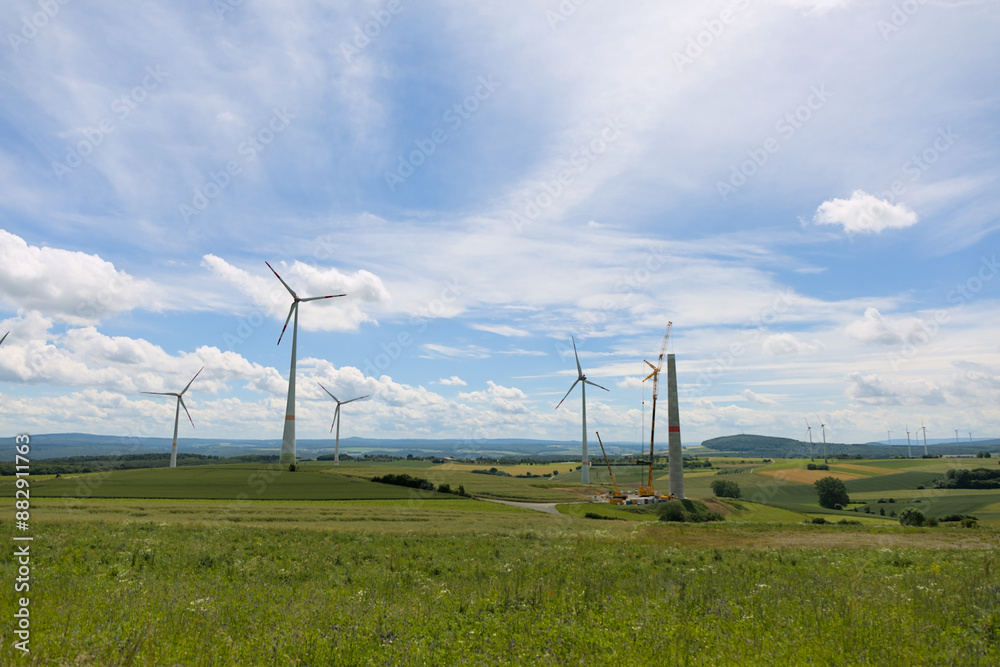 Tower of a wind turbine under construction with a yellow crane in rural landscape. Tower of a wind turbine under construction with a yellow crane in rural landscape.