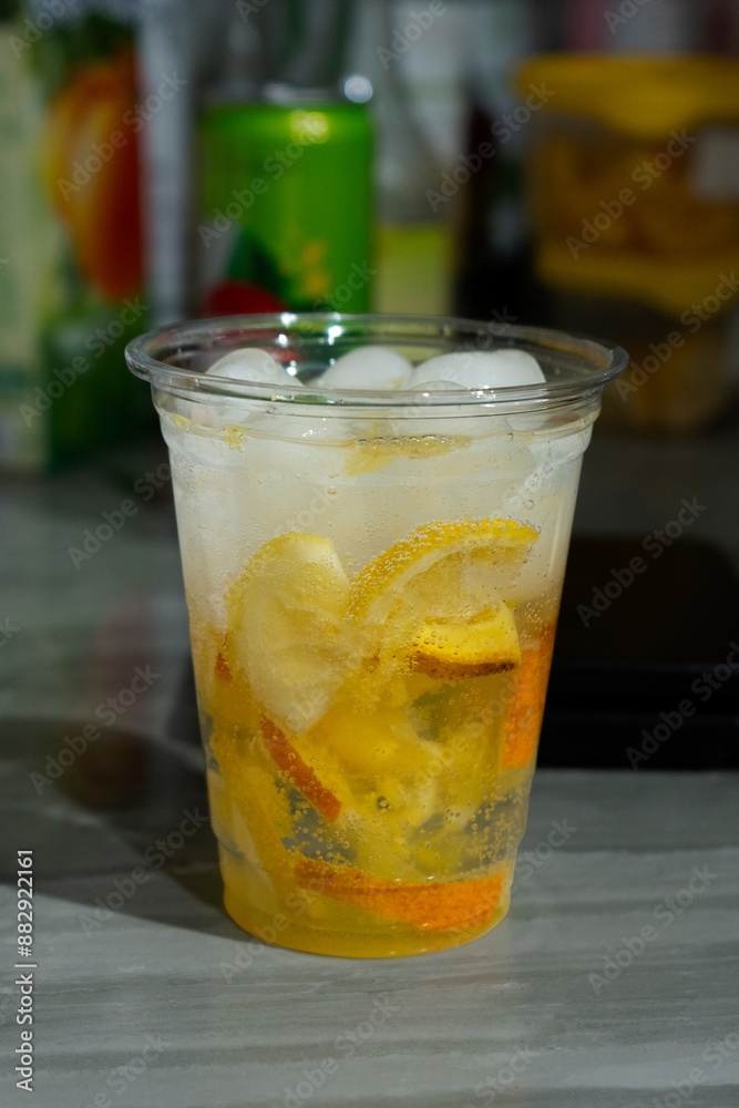 Cold lemonade with ice and fresh citrus pieces in a transparent plastic glass. Cold citrus mojito. Refreshing bright summer drink close-up. Cold lemonade with ice and fresh citrus pieces in a transparent plastic glass. Cold citrus mojito. Refreshing bright summer drink close-up.
