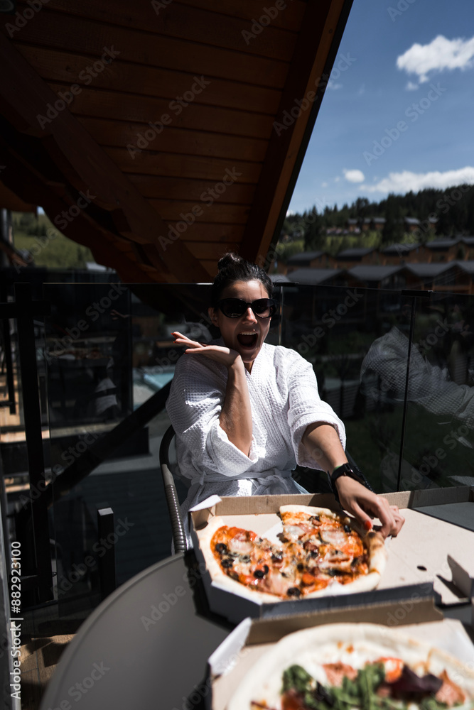 A woman in a bathrobe eats pizza on a balcony overlooking the mountains. Hotel holiday concept. Pizza A woman in a bathrobe eats pizza on a balcony overlooking the mountains. Hotel holiday concept. Pizza