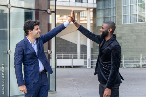 Canvas Print black African businessman in suit fist bumps Hispanic counterpart in city financ