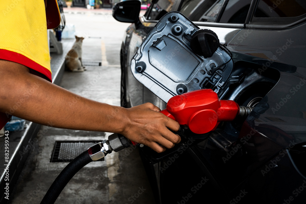 Attendant in uniform at the gas station, filling with petrol a small car, nozzle is in the tank Attendant in uniform at the gas station, filling with petrol a small car, nozzle is in the tank