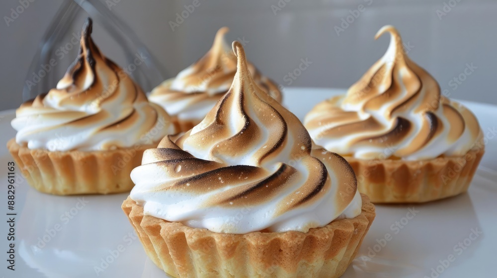 Four mini lemon meringue tarts with toasted meringue on a white plate. Four mini lemon meringue tarts with toasted meringue on a white plate.