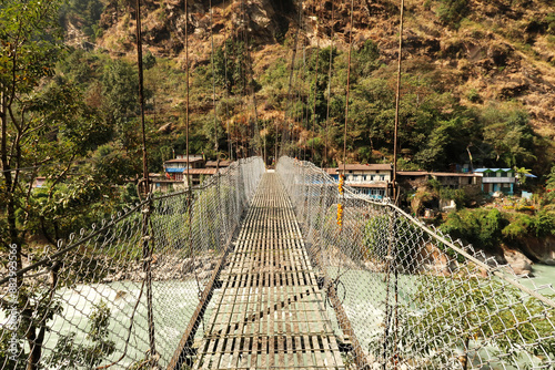 Crossing the metal suspension bridge over the Marsyangdi River leading into Syanche village, Annapurna Circuit Trek, Nepal photo