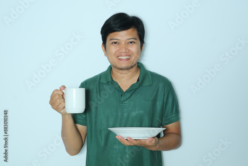 Young Asian man smiling happy while holding a white cup and empty dinner plate. Wearing a green t-shirt photo