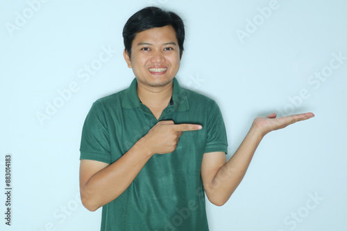 Young Asian man smiling while pointing to his open left hand palm. Wearing a green t-shirt photo