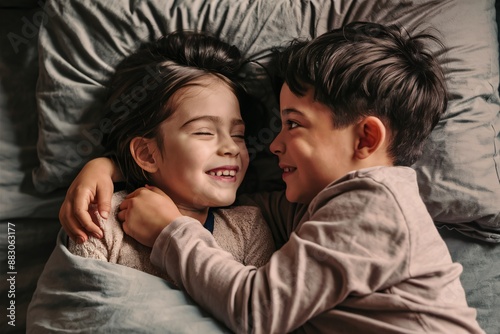 A boy and a girl are lying in bed together. They are both smiling and look happy.