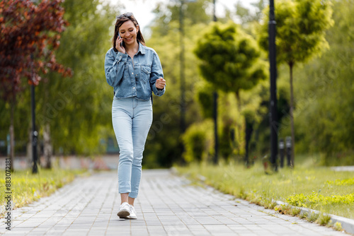 Woman in Denim Shirt Walks and Talks on Phone in Park