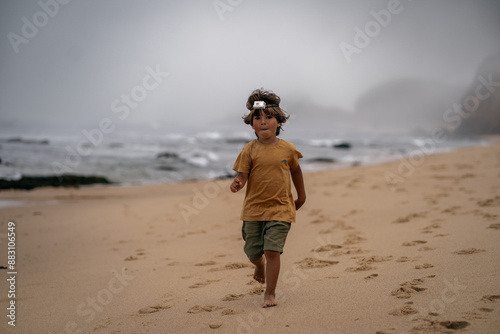 cute happy boy in a headlamp running fast on the beach with the background of the sea in the fog