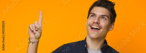 A young man, with a bright smile and a raised forefinger, looks up towards an empty space as if he has just had a brilliant idea