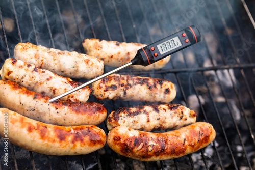 Close-up shot of digital meat thermometer with Fahrenheit scale showing safe cooking temperature inside of grilling turkey sausages on smoking barbecue photo