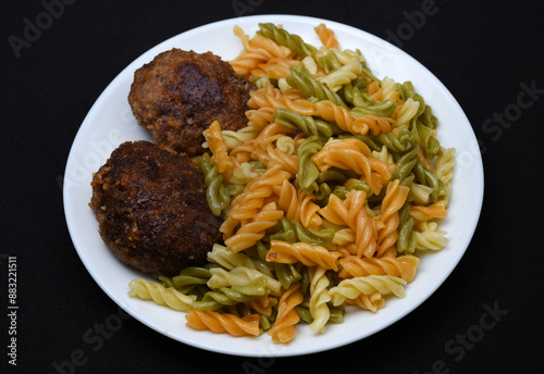 Multicolored pasta on a white plate with cutlets. Meat cutlets with pasta. A hearty lunch.