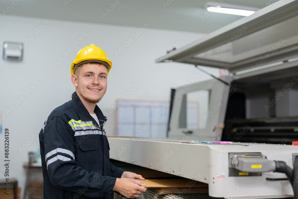 Male engineer checking quality cardboard box parts cutting from laser CNC machine in paper factory. Man technical in uniform wearing helmet safety operate and maintenance machine