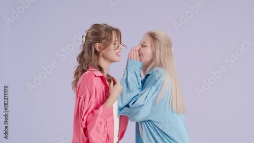 Young stylish women models posing and whispering gossiping and laughing, isolated on purple background. Fashion and youth beauty concept.