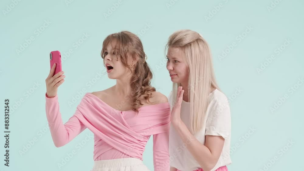 Young fashionable women models talking chatting by video call on smartphone, isolated on blue background. Fashion and youth beauty concept. Young fashionable women models talking chatting by video call on smartphone, isolated on blue background. Fashion and youth beauty concept.