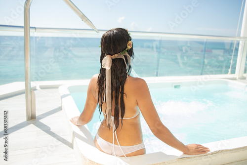 Sexy tourist in white swimsuit inside a jacuzzy pool relaxing and enjoying the Caribbean Sea in the background, with its crystal clear turquoise waters warmed by the radiant Caribbean sun. photo