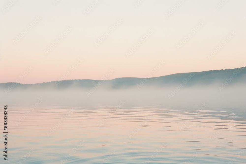 Fototapeta premium Tranquil Misty Lake at Sunrise with Hazy Hills in the Distance