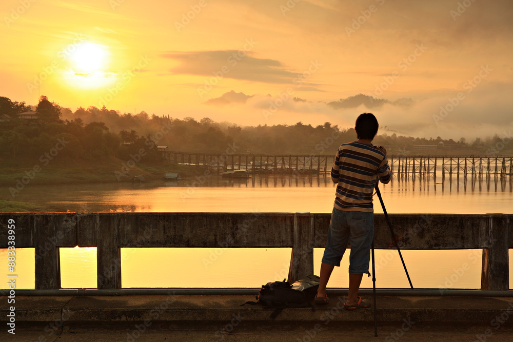 Fototapeta premium A Photographer take picture Wood bridge with river and mountain in Sangkhla buri, Kanchanaburi province, Thailand 