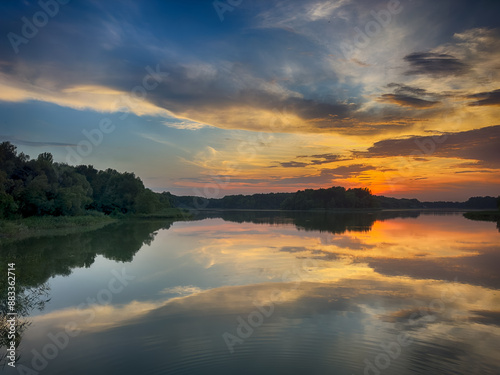 Serene Fishing Lake: A peaceful scene by the tranquil waters of a secluded fishing lake. Surrounded by lush greenery and framed by a clear blue sky, this picture captures the essence of a perfect day 