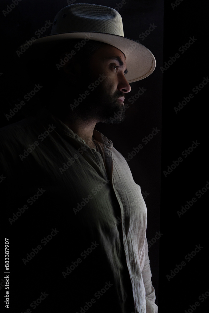 Portrait of a handsome bearded man in a shirt and white hat. A man looks into the distance in the dark. Vertical photo. High quality photo Portrait of a handsome bearded man in a shirt and white hat. A man looks into the distance in the dark. Vertical photo. High quality photo