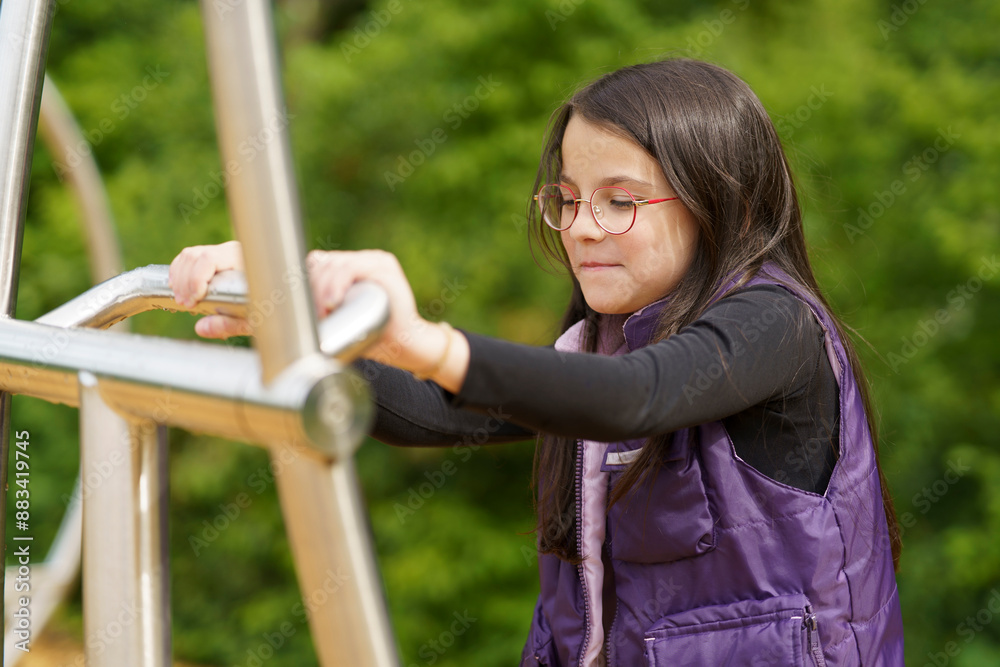 Naklejka premium A little cute smiling girl in glasses and a purple vest plays on the playground. Happy childhood concept