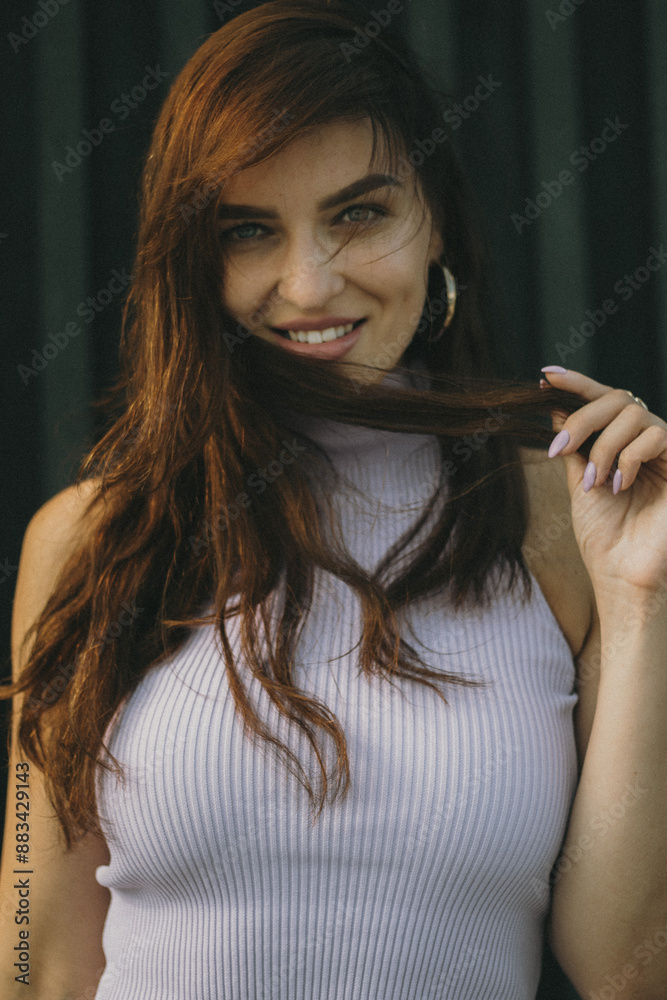 Obraz premium Woman with long hair and hoop earrings, wearing a lavender top, gently touching her hair while posing against a dark background.