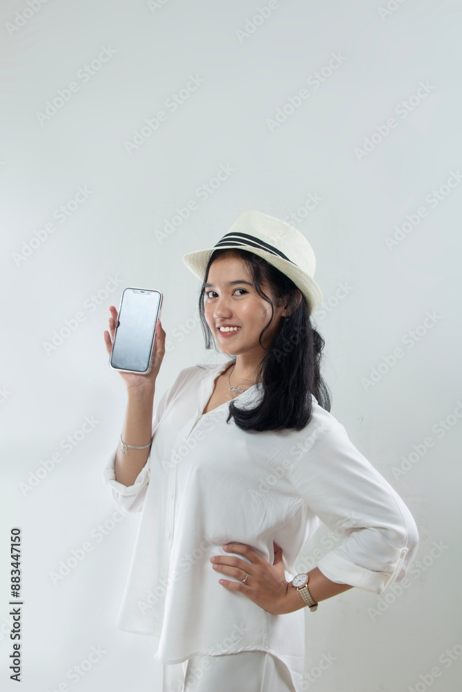 Beautiful young Asian woman tourist in straw hat standing surprised in her white clothes holding mobile phone and showing phone to front camera, young people advertising buy tickets online, isolated w Beautiful young Asian woman tourist in straw hat standing surprised in her white clothes holding mobile phone and showing phone to front camera, young people advertising buy tickets online, isolated w