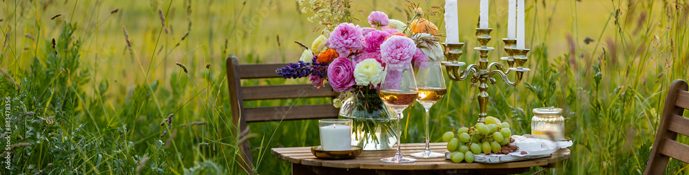 Elegant wedding or private party for a loving couple table setting outdoors in the garden. Beautiful decor with fresh ranunculi flowers, candles. Gourmet cheese board, fruits, white wine. Banner Elegant wedding or private party for a loving couple table setting outdoors in the garden. Beautiful decor with fresh ranunculi flowers, candles. Gourmet cheese board, fruits, white wine. Banner