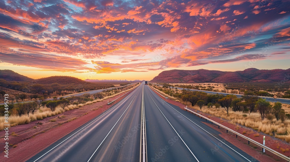 A multi-lane highway situated in the Australian outback, framed by colorful clouds and a vivid dusk sky A multi-lane highway situated in the Australian outback, framed by colorful clouds and a vivid dusk sky