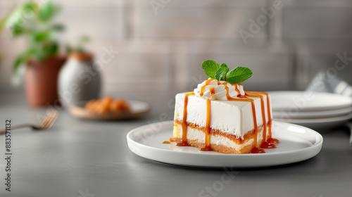 A slice of tres leches cake covered in whipped cream, drizzled with caramel sauce, and garnish with a mint leaf, on a white plate.
