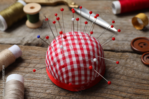 Checkered pincushion with pins and other sewing tools on wooden table, closeup photo