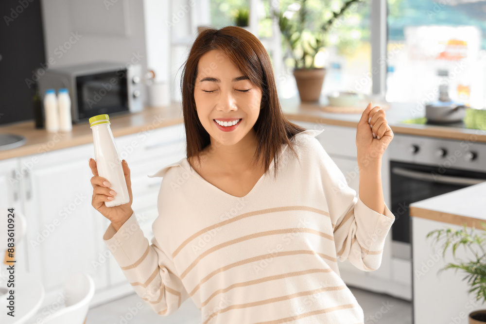 Happy young Asian woman with bottle of tasty yogurt at home Happy young Asian woman with bottle of tasty yogurt at home