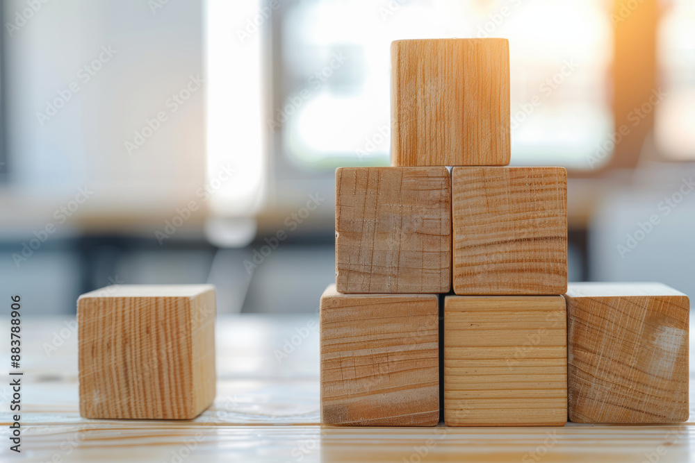 Wooden blocks stacked in a pyramid shape on a light wooden table with a blurred background, sunlight streaming through a window, creating a warm ambience. Wooden blocks stacked in a pyramid shape on a light wooden table with a blurred background, sunlight streaming through a window, creating a warm ambience.