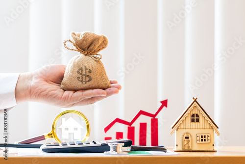 Businessman hand hold the money bag and magnifying glass searching a home and red arrow and bar graph and calculator and agreement in the office, Loan for real estate to family in the future concept.