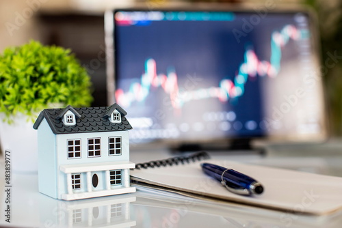 House model, pen and notepad on table with stock market chart, real estate market photo